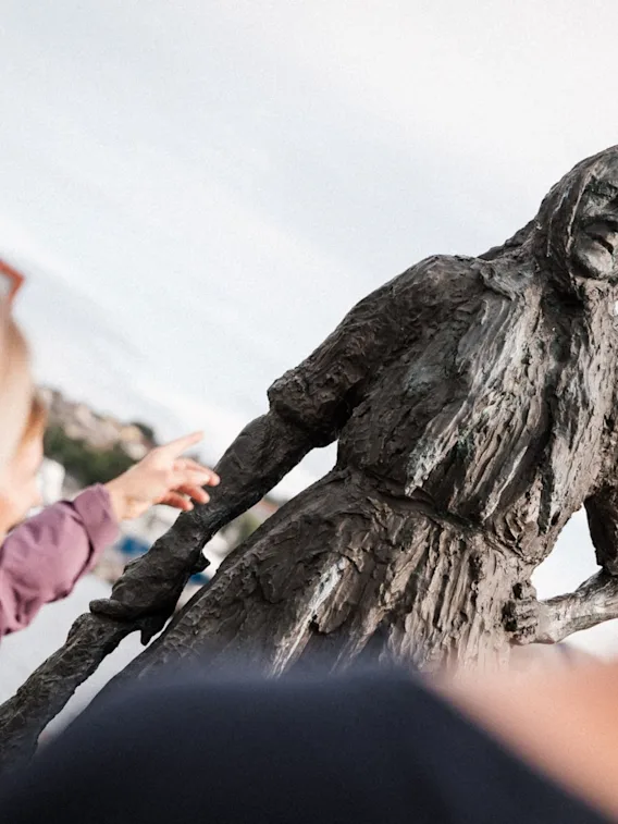 En turist som peker mot bronsestatuen Klippfiskkjerringa i Kristiansund.
