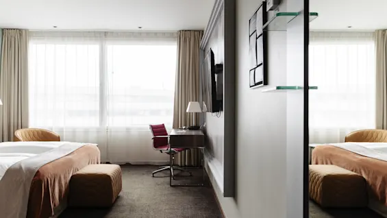 Ett ljust och modernt hotellrum med två bekväma sängar, en skrivbordsplats och ett stort fönster, perfekt för avkoppling eller arbete.