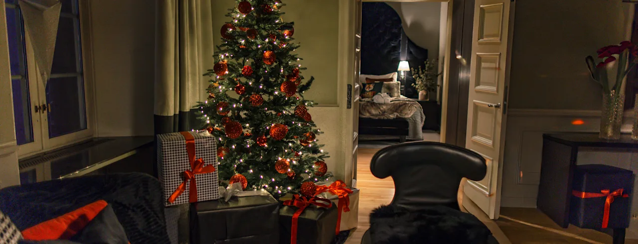 Et varmt og indbydende rum dekoreret til helligdagene, med et glødende juletræ og gaver, med et kig ind i et behageligt soveværelse.