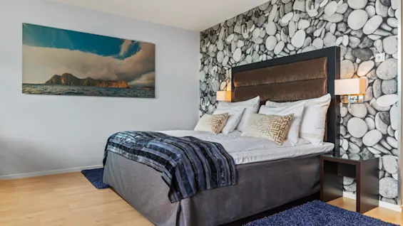 Ett bekvämt och stilfullt sovrum på Quality Hotel Ulstein, med en stor säng, en naturskön målning och en accentvägg med stenmönster.