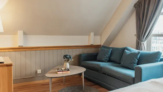 A cozy living area with a blue sofa, coffee table, and sloped ceiling, perfect for relaxation.