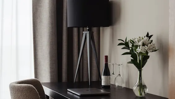 Et stilrent hotellrom med skrivebord, laptop, vin og blomster, klart for arbeid eller avslapning.