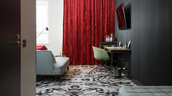 A stylish room with red velvet curtains, a desk with a chair, and a couch, showcasing modern interior design.