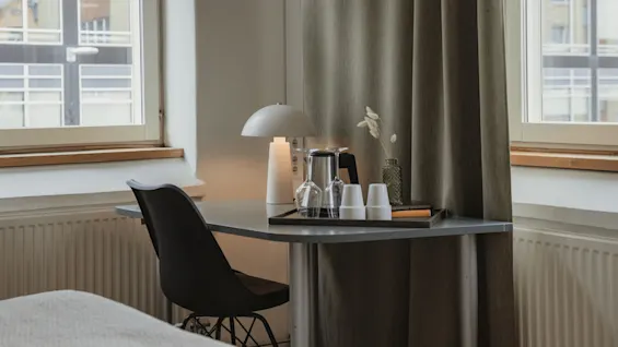 A well-lit desk area in a room at Home Hotel Uppsala, featuring a lamp, glasses, and a comfortable chair by a window.