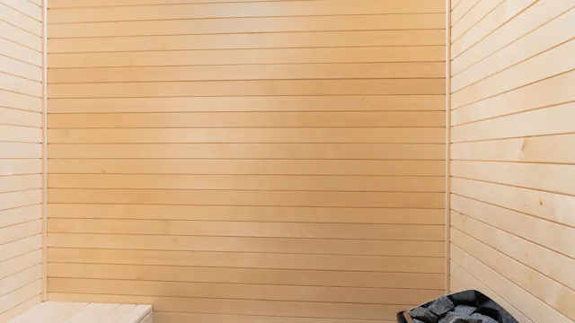 A wooden sauna room with sleek, horizontal paneling. A heater with dark stones is on the right, and a bench is on the left, set against tiled flooring.