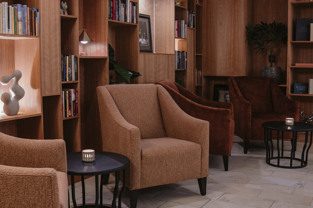 En varm och inbjudande hotellounge med bekväma sittplatser, bokhyllor och mjuk belysning. En bok med titeln Playing Cards är synlig.
