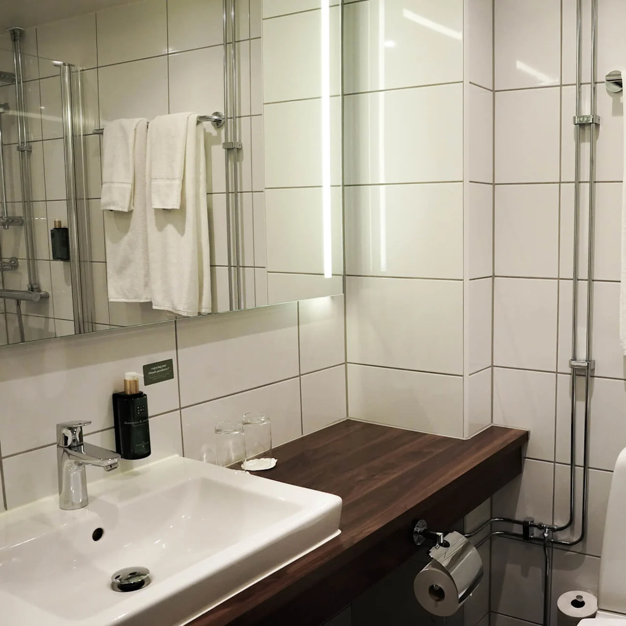 A modern bathroom with a sink, towel rack with two towels, and a shower area reflected in a mirror.