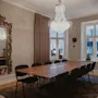 Muodollinen kokoushuone, jossa on pitkä puupöytä, mustat tuolit, koristeellinen peili ja kimalteleva kattokruunu.