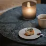En koselig scene med et kakestykke, en kopp kaffe og et tent lys på et marmorbord, som antyder en avslappende pause.