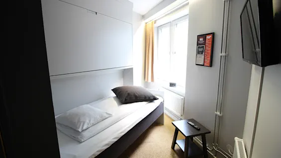 Valoisa ja kompakti hotellihuone, jossa on yhden hengen sänky, pieni sivupöytä ja luonnonvaloa tuova ikkuna.