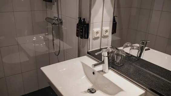 Ett rent och modernt hotellbadrum med handfat, spegel och duschplats, redo för gästanvändning på Home Hotel Grand, Helsingborg.