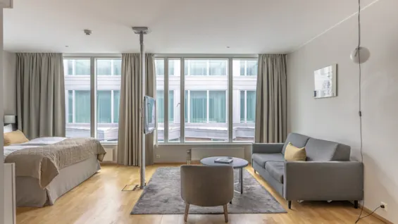 A bright and modern hotel room featuring a comfortable bed, a cozy seating area with a sofa, and large windows.