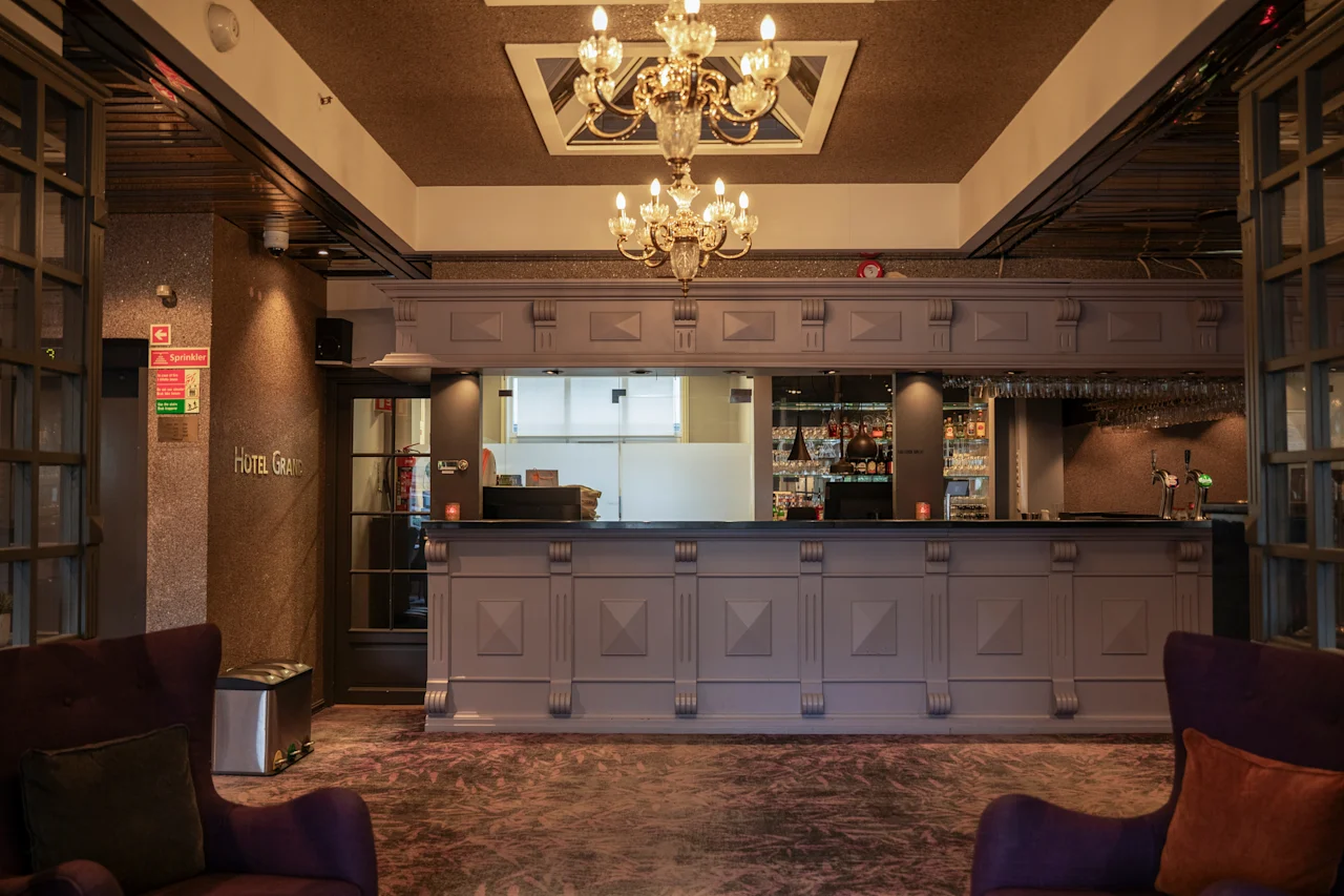 En luksuriøs hotellobby med en storslået reception, elegante lysekroner og komfortable siddepladser. Synlig tekst: Hotel Grand.