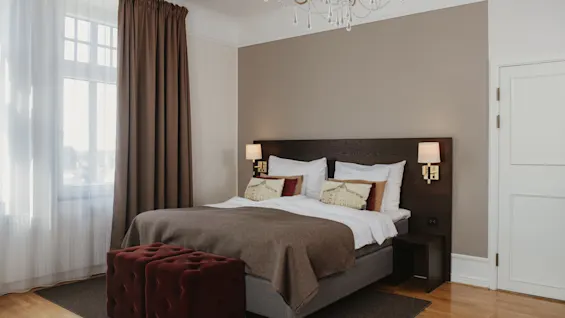 Mukava hotellihuone, jossa on tilava sänky, tyylikäs kattokruunu ja pehmeä valaistus rentouttavaan oleskeluun.