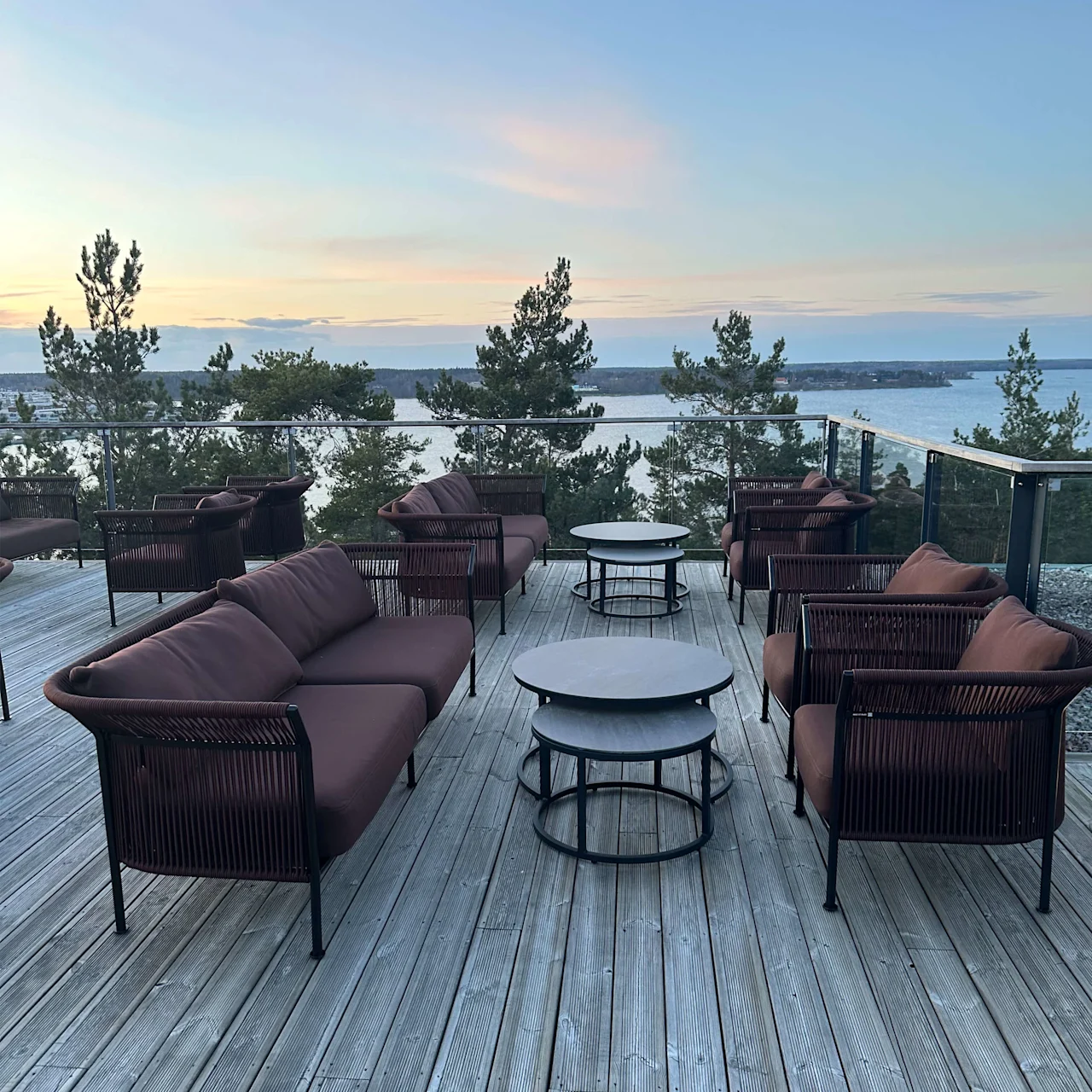 Utemøbler er arrangert på en treterrasse som ser ut over en idyllisk innsjø i skumringen.