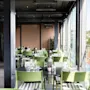 En lys, moderne restaurant med grønne stoler, mørke bord og store vinduer med utsikt over en by.