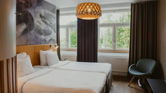 A bright and inviting twin room at Home Hotel Uppsala, featuring two comfortable beds, a large window, and a unique light fixture.