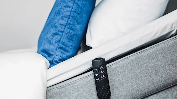 Adjustable bed angled upward, with a blue pillow, a white pillow, and a remote control attached to the side. Bedroom setting.