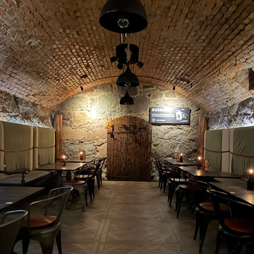 En hyggelig, dæmpet oplyst hvælvet murstenskælderrestaurant med borde, stole og levende lys, med et skilt der læser BIERHALLE.