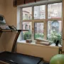 An indoor fitness area with a treadmill by a window, offering a view of urban buildings and greenery.