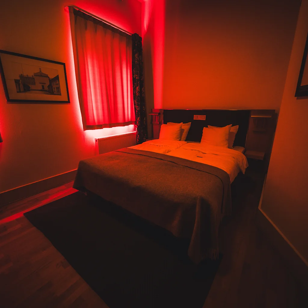 Ett mysigt sovrum på Home Hotel Bilan, upplyst av ett varmt rött sken bakom gardinerna, vilket skapar en unik atmosfär.