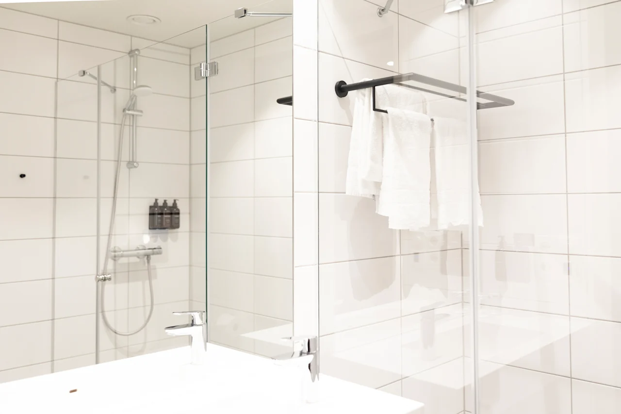 Valoisa ja toimiva kylpyhuone, jossa on kaakeloitu suihkutila, tyylikäs pesuallas ja siististi ripustetut valkoiset pyyhkeet.