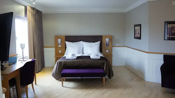 A neatly made double bed in a clean, well-lit hotel room with modern furnishings and artwork on the walls. 