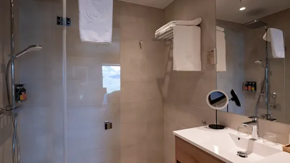 Ett rent och modernt hotellbadrum med en dusch bakom glas och en kommod med spegel och rena handdukar.