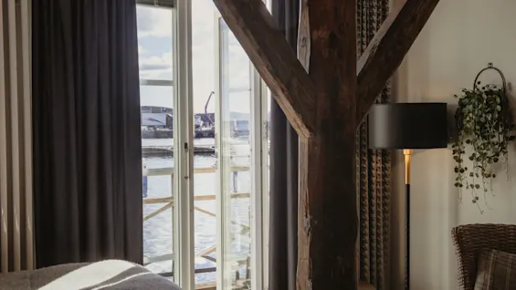 Et hyggeligt værelse med et stort vindue med udsigt over en havn, med en rustik træbjælke og varm belysning.