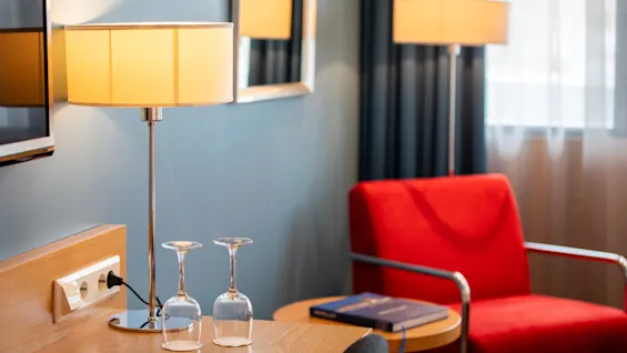 Et komfortabelt hotellrom på Quality Hotel Ulstein med en varm lampe, to glass og en rød lenestol ved vinduet.
