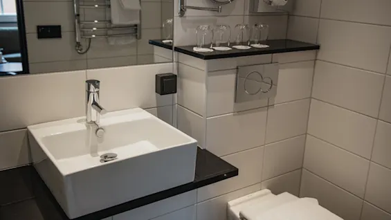 Valoisa ja moderni kylpyhuone, jossa on tyylikäs pesuallas, suuri peili, wc, puhtaat pyyhkeet ja juomalasit hyllyllä.