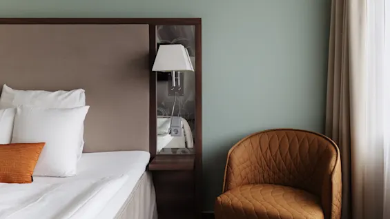 Et hyggeligt hotelværelse med en seng, en sengelampe og en komfortabel lænestol, med et moderne og indbydende design.