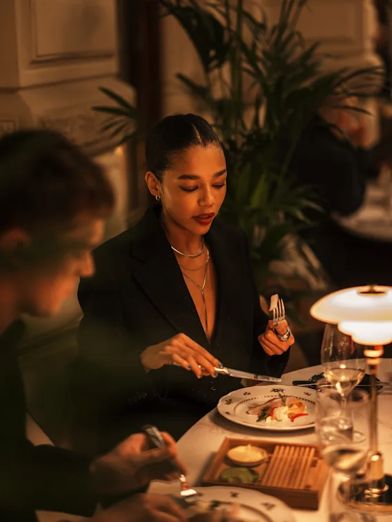 En person i en dempet belyst restaurant skjærer mat på en tallerken med kniv og gaffel, nyter et måltid.