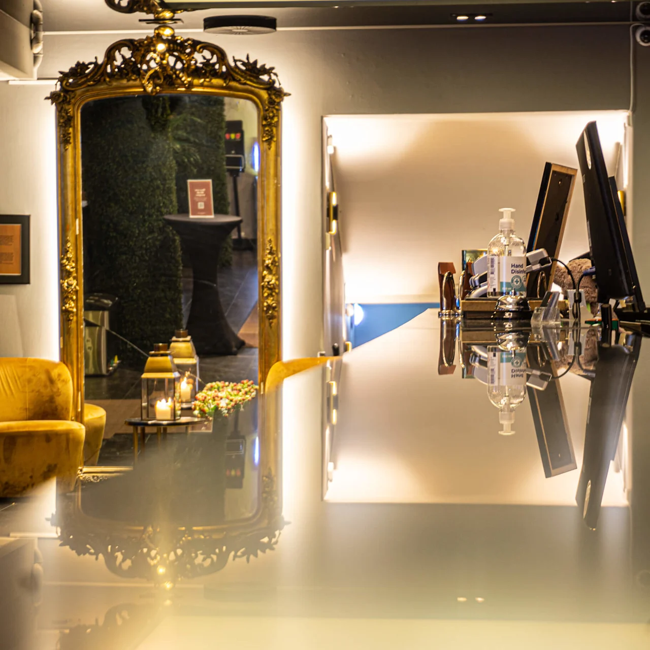 Elegant interior with a yellow armchair, ornate mirror, and modern desk holding various items, bathed in warm light.