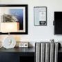 Et hotelværelses skrivebordsområde med en lampe, radio og et indrammet kystlandskabsbillede. En vægskærm viser Få fordele.