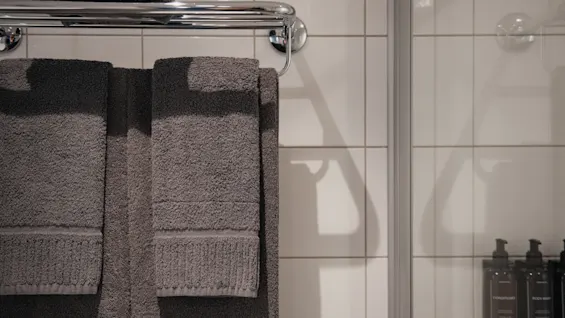 Färska handdukar hänger på en ställning bredvid en dusch med flaskor för balsam och kroppstvål, redo att användas.