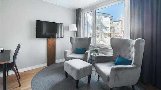 Two grey armchairs with blue cushions, centered in a modern living room with a mounted TV and large window.