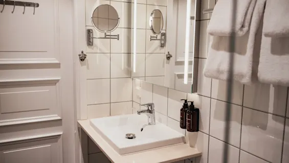 Ett välutrustat hotellbadrum med ett rent handfat, en belyst spegel och fräscha vita handdukar redo att användas.