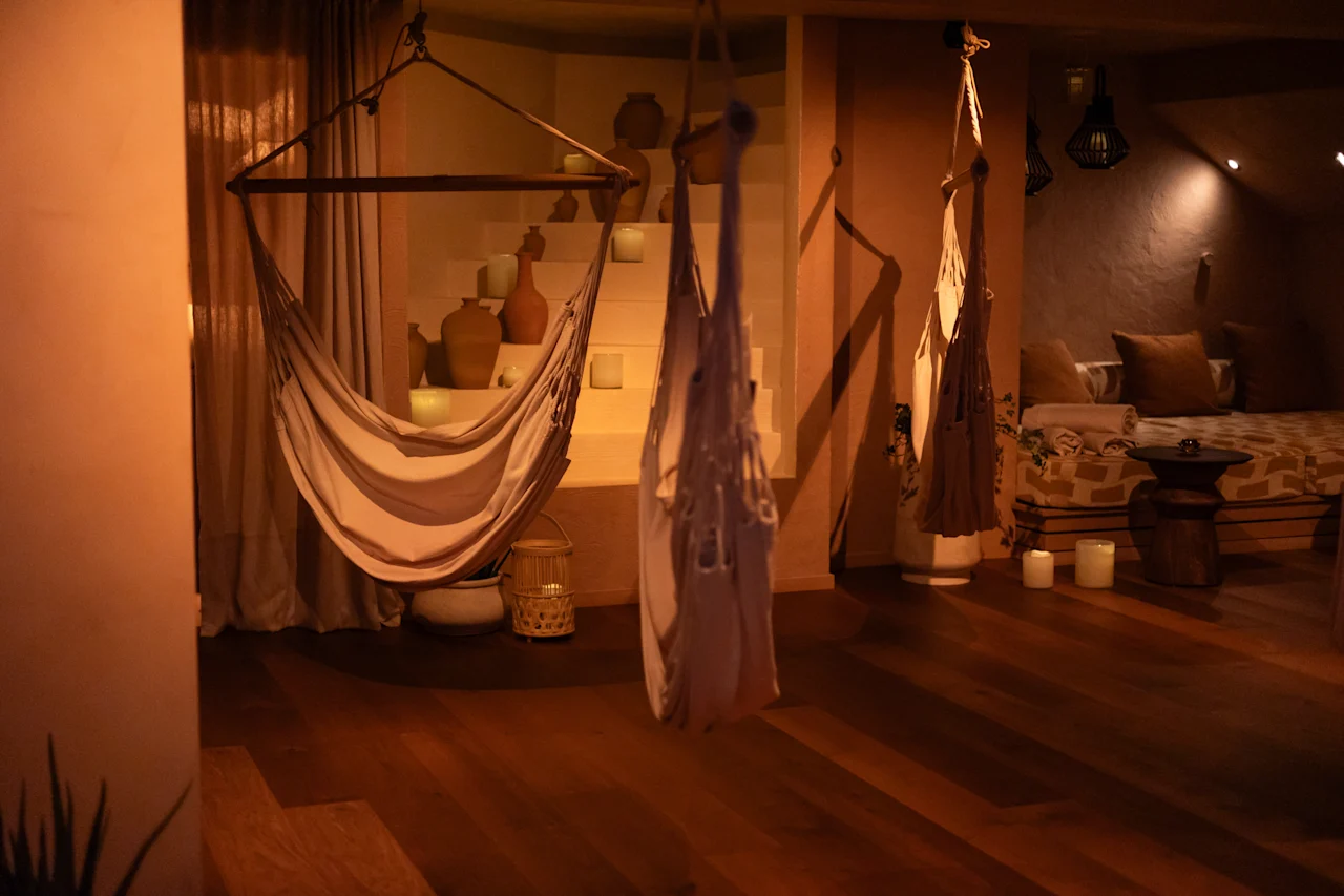 Rauhallinen, hämärästi valaistu huone, jossa on riippumattoja, hehkuvia kynttilöitä ja koristeellisia maljakoita, luoden rauhallisen ja rentouttavan tunnelman.