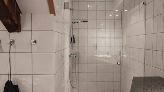 Et rent og moderne bruseområde med hvide flisevægge, en glasvæg og et mørkt gulv, klar til brug.