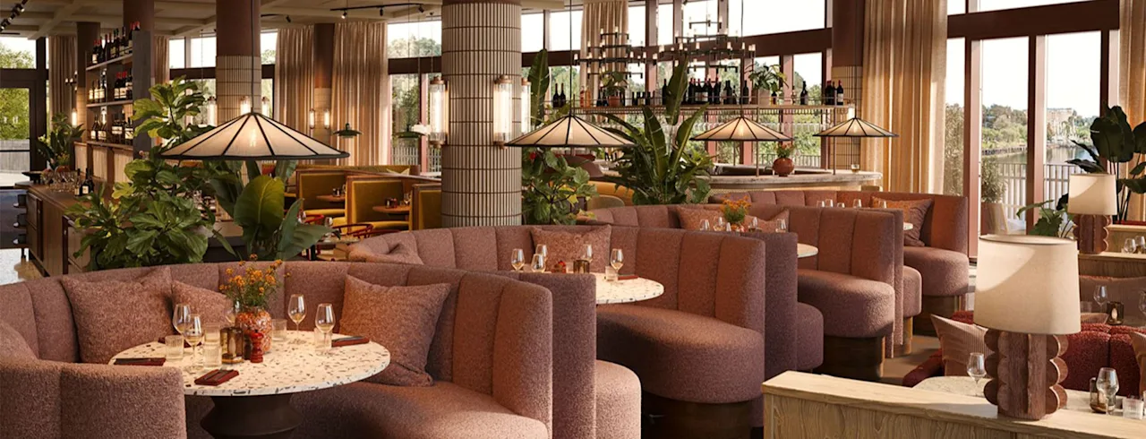 Bekväma böjda bås prydda med glas och blommor finns i en varmt upplyst restaurang med stora fönster, inomhusväxter och hängande lampor, vilket skapar en mysig matmiljö.