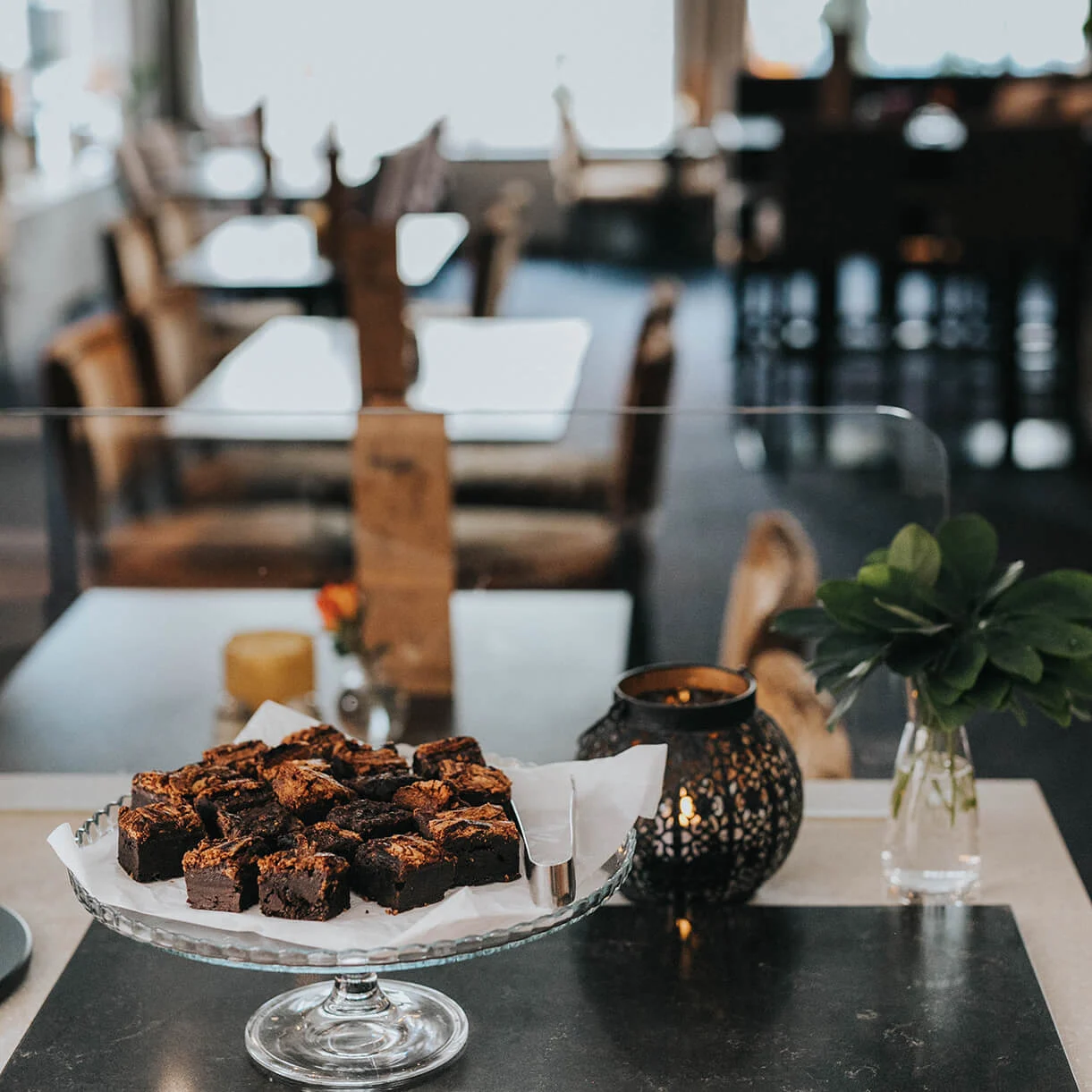 En tallerken med brownies er centreret på et bord inde i en hyggelig café med stole og dekorative genstande.