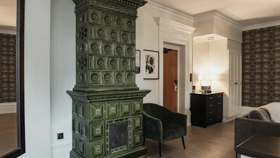 Et koselig interiør på Home Hotel Norre Park i Halmstad med en utsmykket grønn kakkelovn, en lenestol og en sofa.