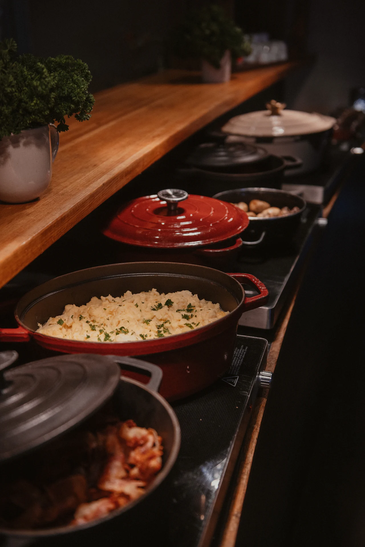 A cozy buffet setup at Home Hotel Uppsala, offering a selection of hot dishes in cast iron pots, including creamy mashed potatoes.