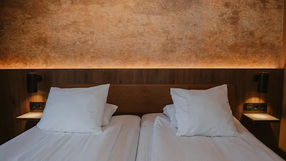 To pent oppredde senger på et hotellrom med en teksturert vegg og myk stemningsbelysning.