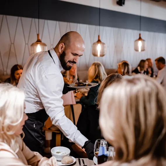 En servitör serverar en måltid till gäster på en livlig restaurang på Quality Hotel Arlanda XPO.