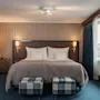 A welcoming hotel room featuring a comfortable bed, stylish plaid ottomans, and a bright window.