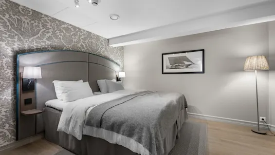 A cozy hotel room with a large bed, patterned wallpaper, and soft lighting, creating a relaxing atmosphere.