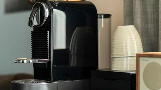 En elegant svart kaffemaskin med kopper og en høyttaler på en overflate, klar for en morgenbrygg.