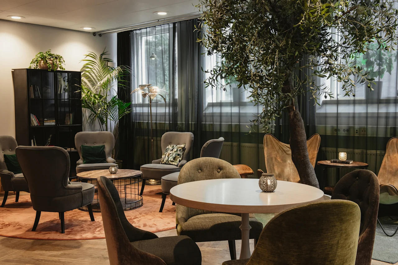 A comfortable and inviting lounge area at Home Hotel Uppsala with various seating, tables, and lush green plants.
